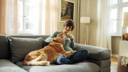 Frau sitzt auf einem Sofa und streichelt einen Hund.