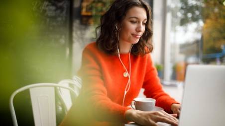 Frau arbeitet mobil von einem Café aus an ihrem Laptop.
