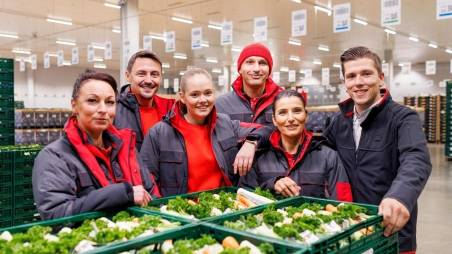 Fünf Logistikmitarbeiter von Kaufland posieren an einer Palette mit Gemüseboxen zum Gruppenfoto.