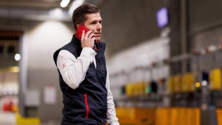 Logistik-Mitarbeiter von Kaufland telefoniert mit seinem Handy beim Gang durchs Lager.